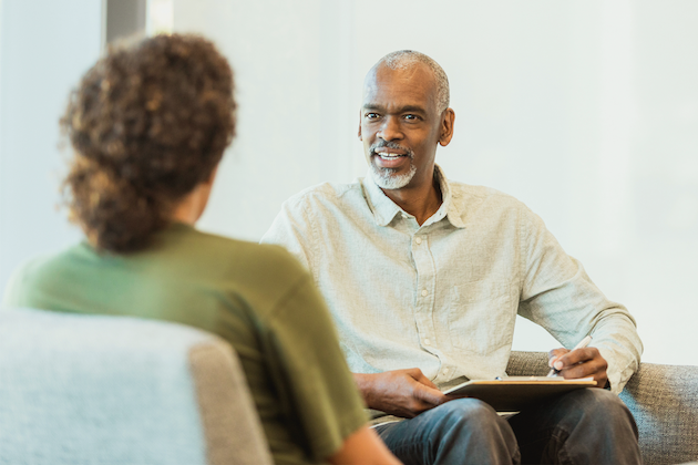 A man holding a notepad in his lap and conversing with someone.