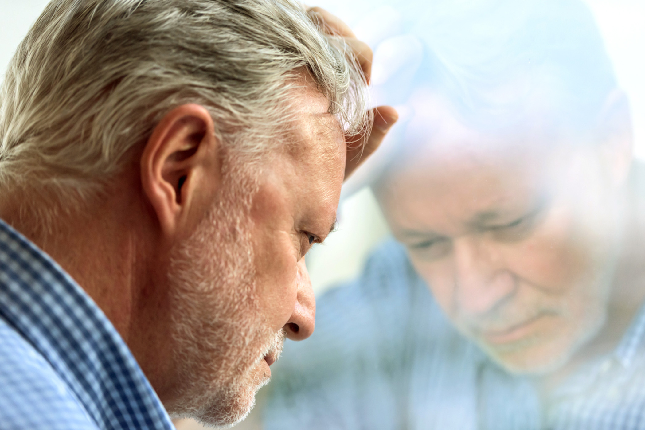 A man with his forehead pressed against a window in deep thought.